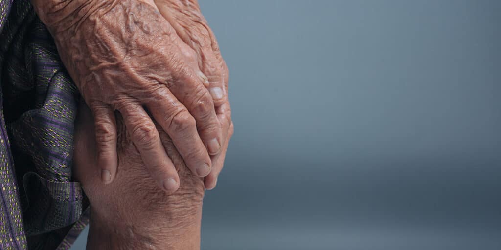 mãos de idosa tocando no joelho com reumatismo