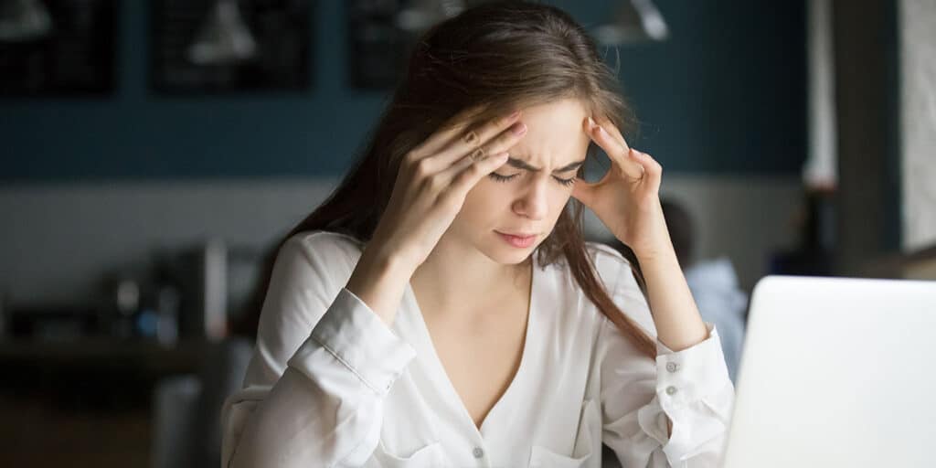 mulher no notebook com dor de cabeça por síndrome antifosfolípide